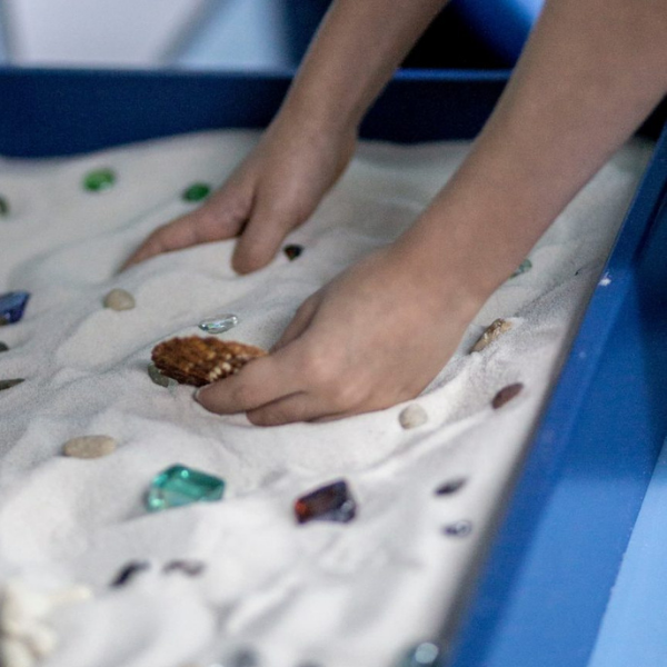 Hands playing with stones and glass cubes in a therapeutic sand tray.